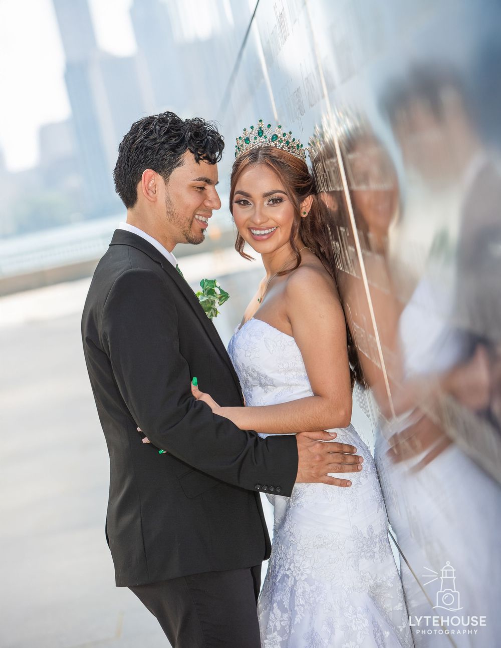A couple poses romantically under a clear umbrella during their wedding photoshoot in an outdoor urban setting.
