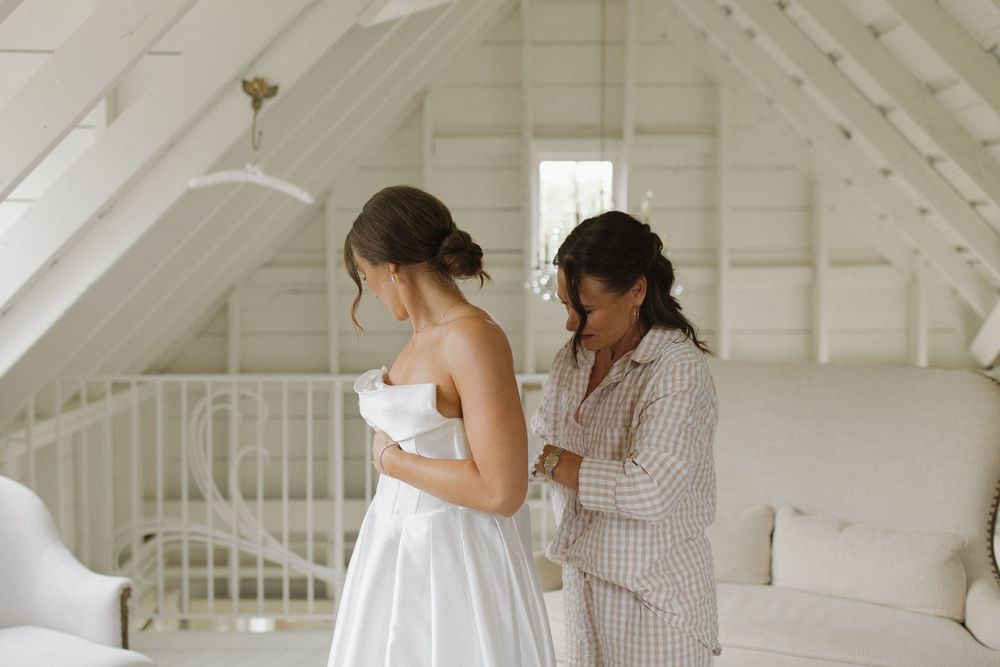 Two people share an emotional embrace in a bright white attic room with exposed beams and a chandelier.