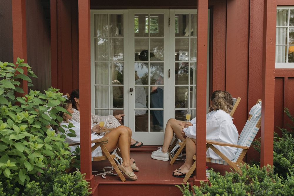 People in white robes relaxing on porch chairs outside red building.