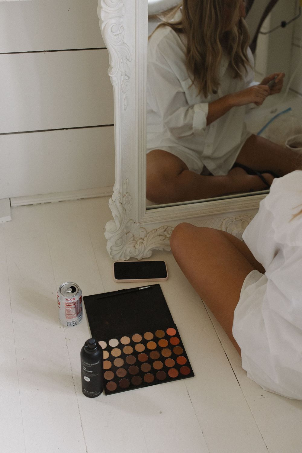 Makeup palette and beauty products on white floor with mirror reflection.
