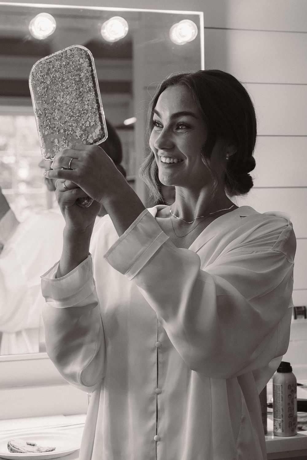 Person in white robe holding mirror during wedding preparation.