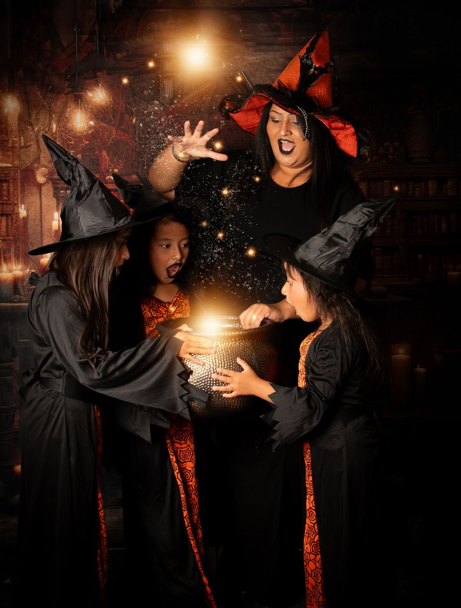 Three witches in black hats and costumes perform magical spells with glowing orbs and sparkles in a spooky setting.