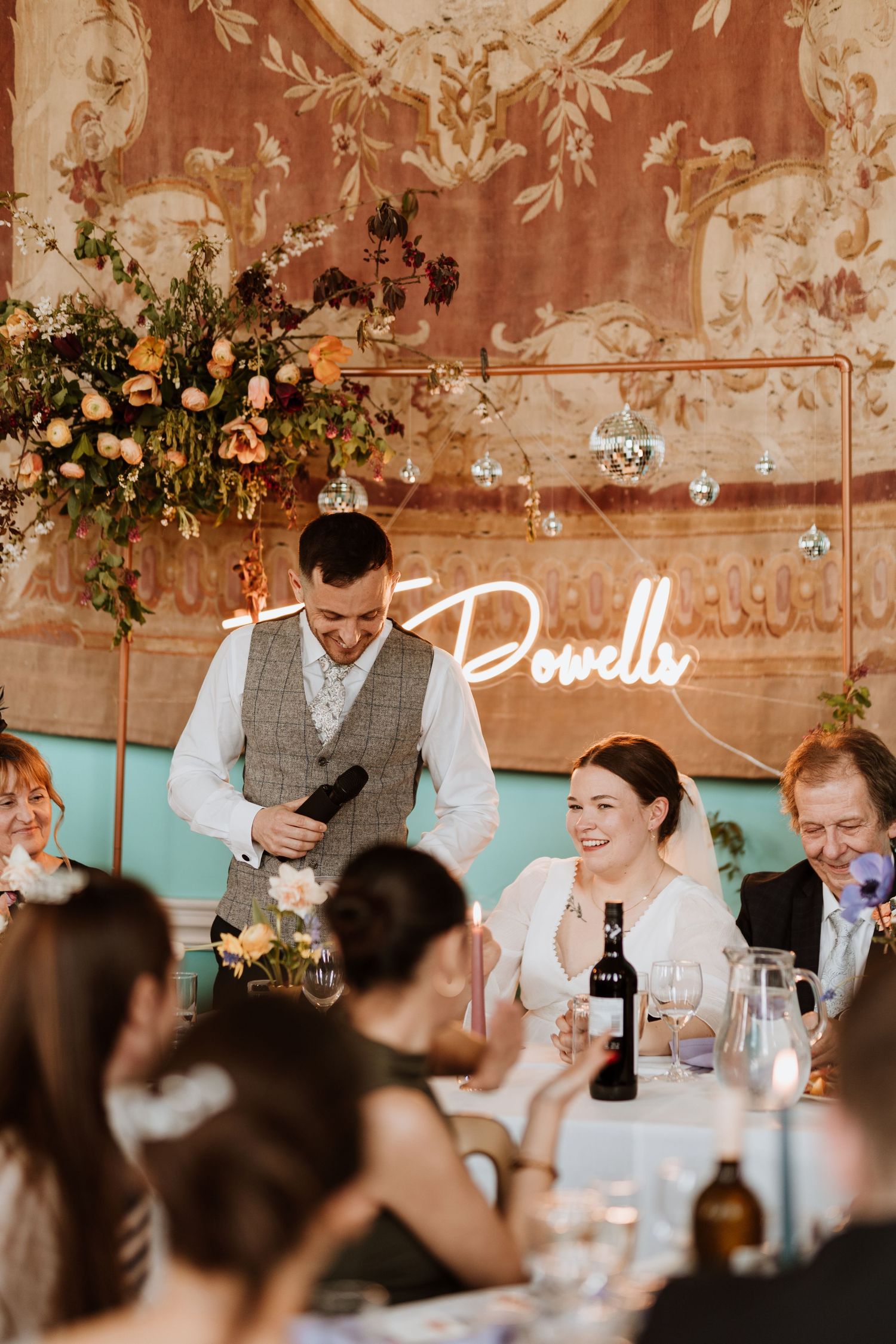 Wedding reception speech during dinner under white tent with string lights and green backdrop at Walcot Hall.