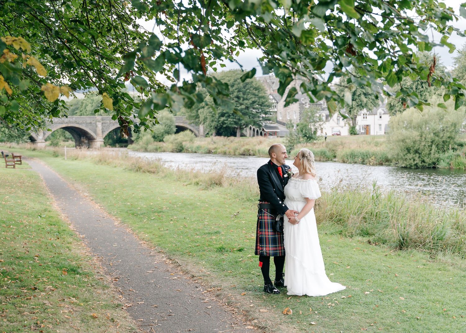 Newlyweds strolling along a scenic pathway surrounded by lush greenery and trees.