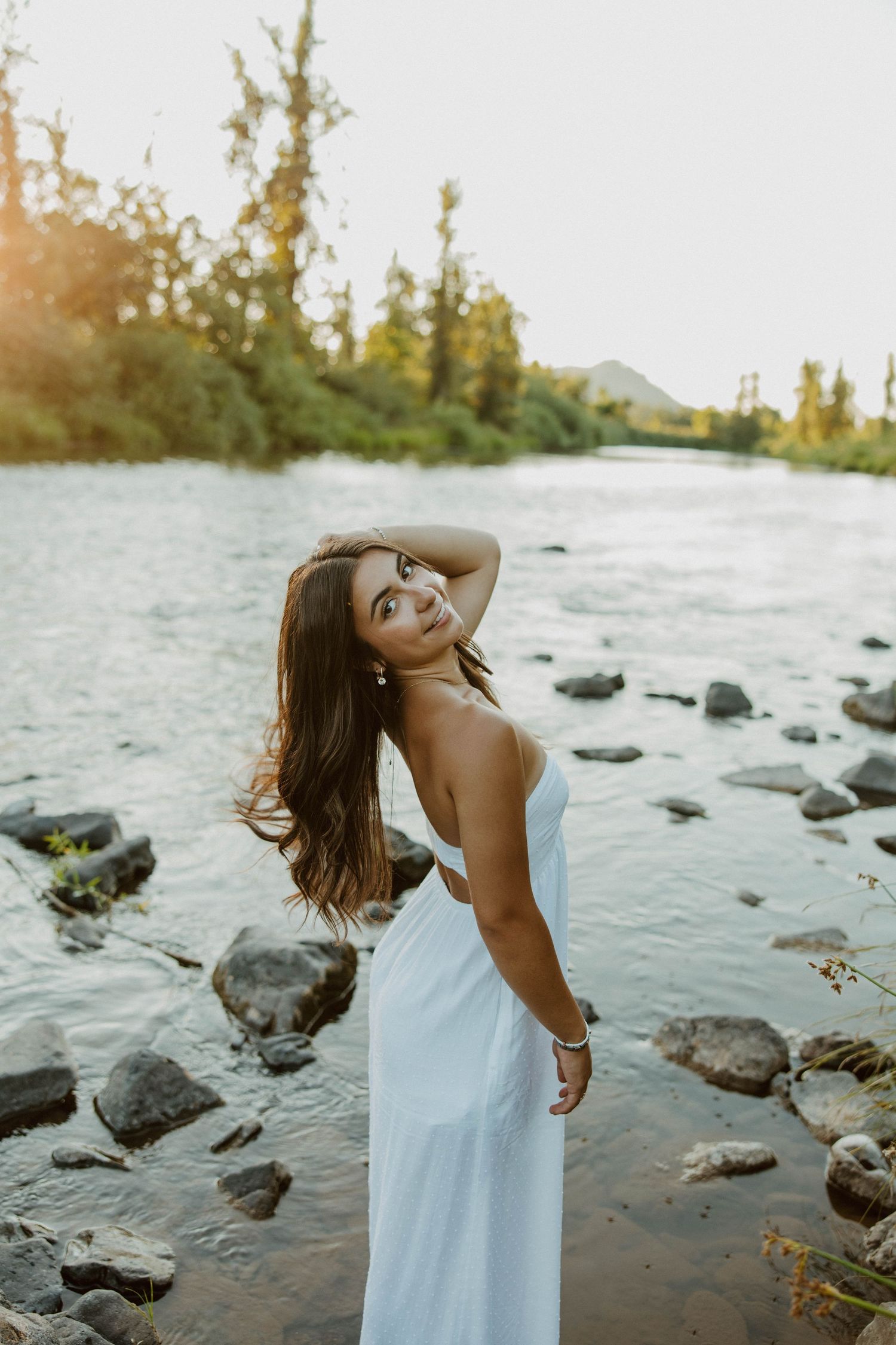 Ethereal portrait session by the water's edge with rocks and golden sunset light.