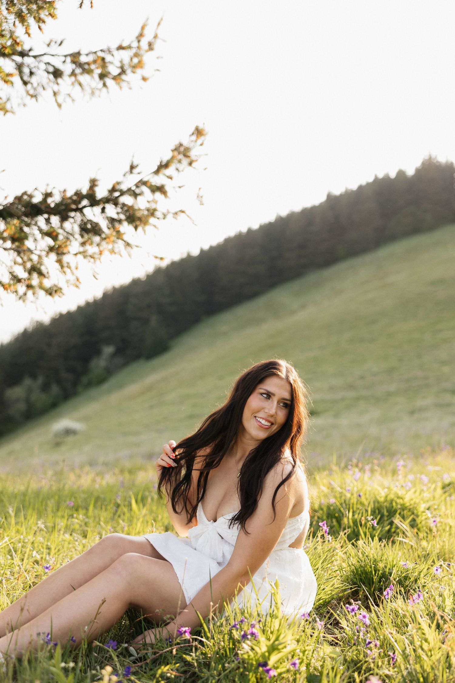 Sunset portrait session in a grassy hillside meadow with mountain backdrop.