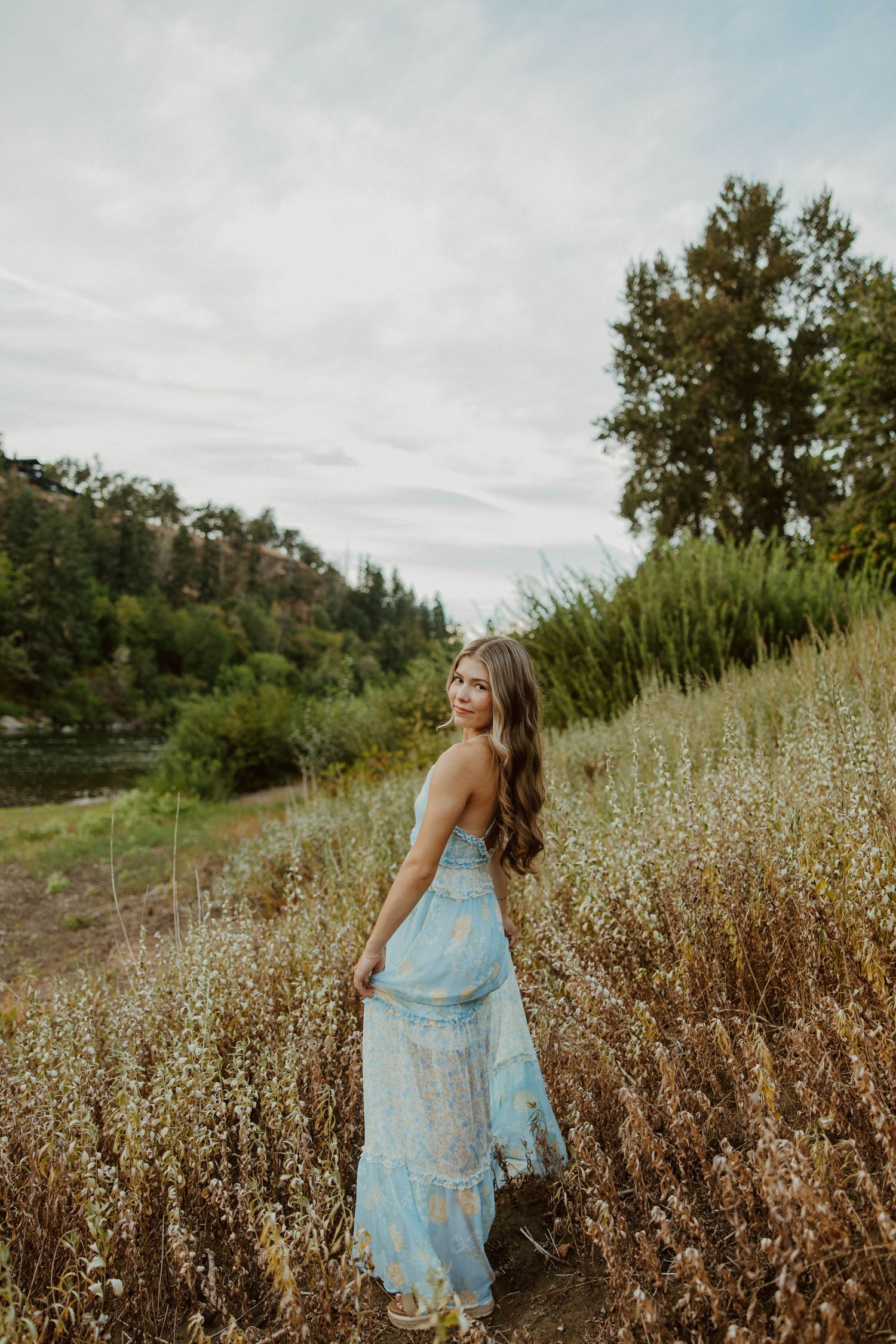 Figure in blue dress walks through dried autumn wildflower field.