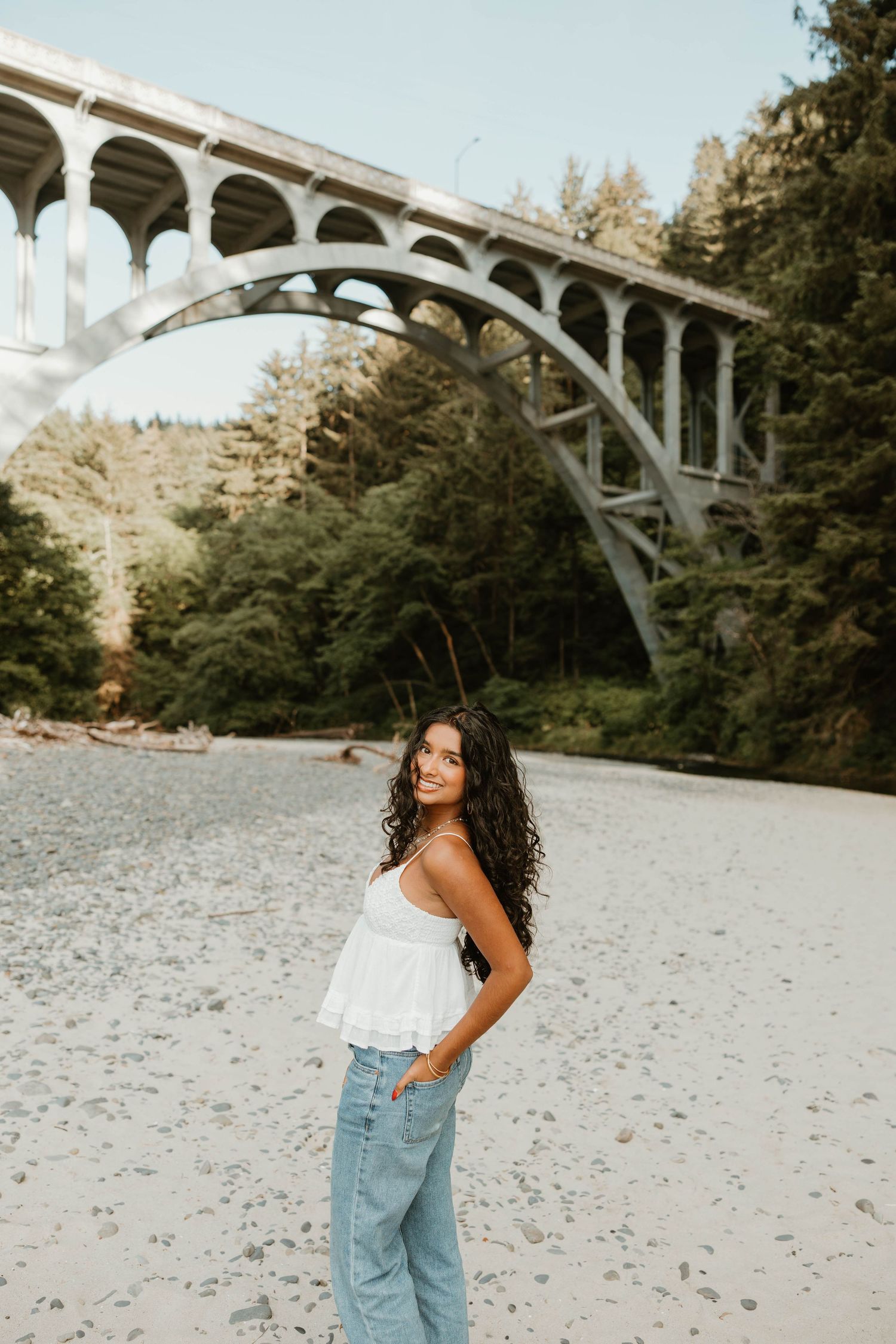 Artistic portrait session beneath a grand concrete bridge on a rocky beach.