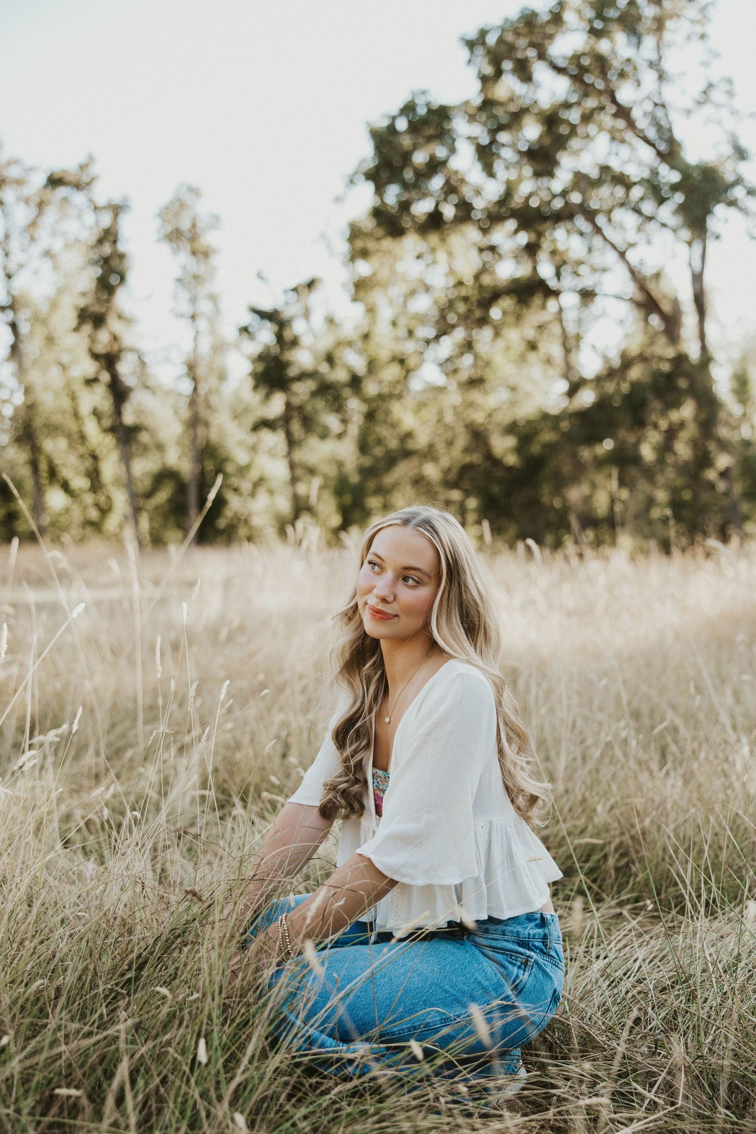 A figure in white sits gracefully in a sun-drenched field of tall grass.