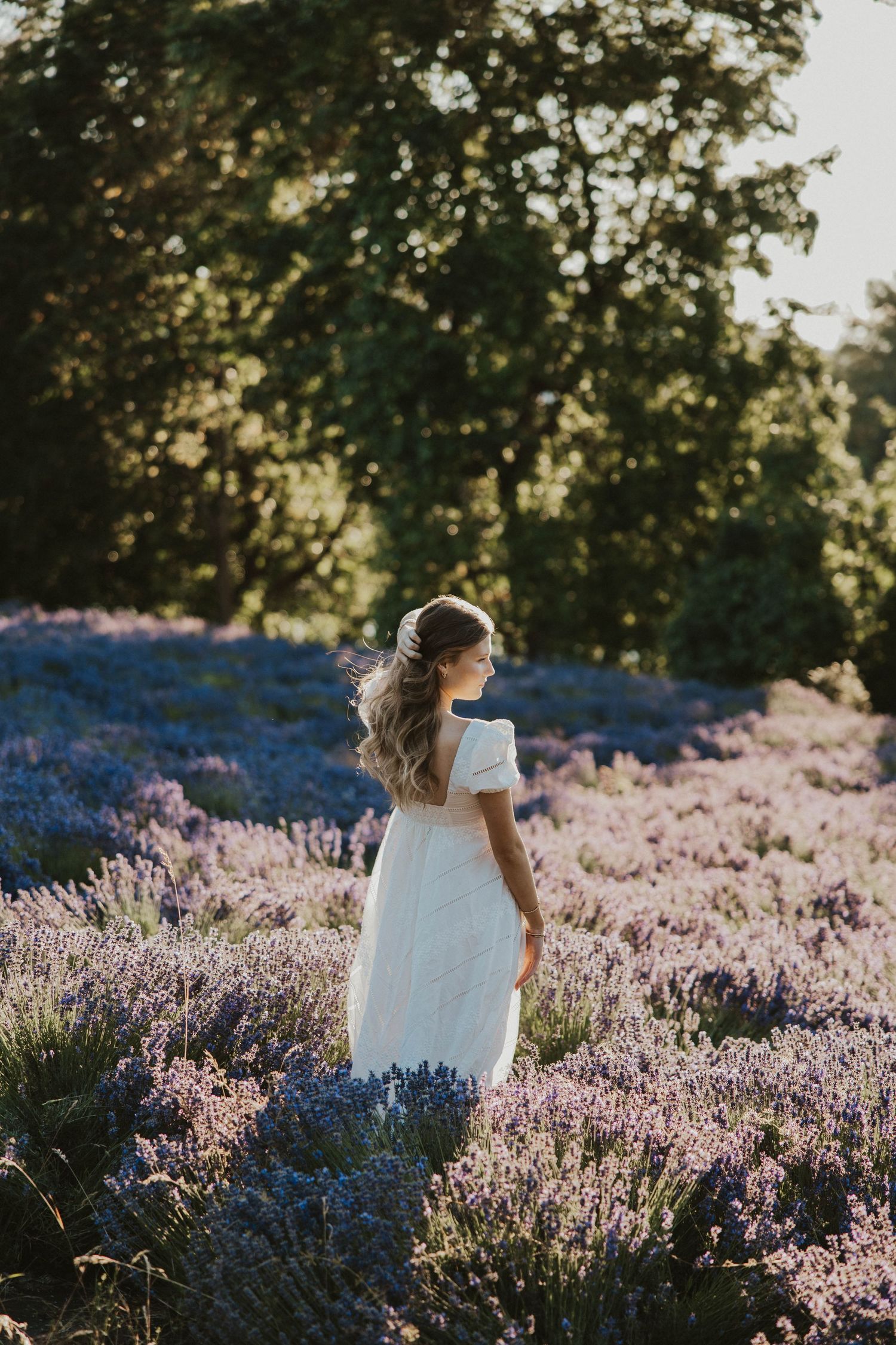 White dress contrasts beautifully against a field of blooming purple lavender at sunset.