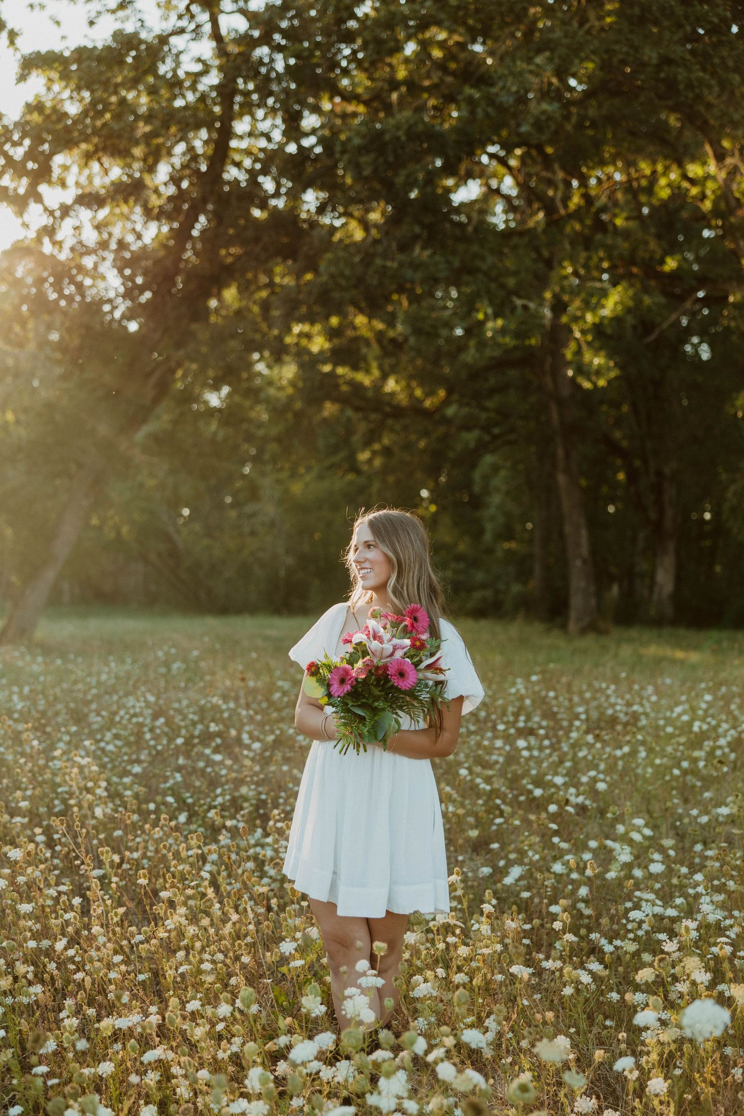 A flowing white dress stands out among a field of delicate white wildflowers at sunset.