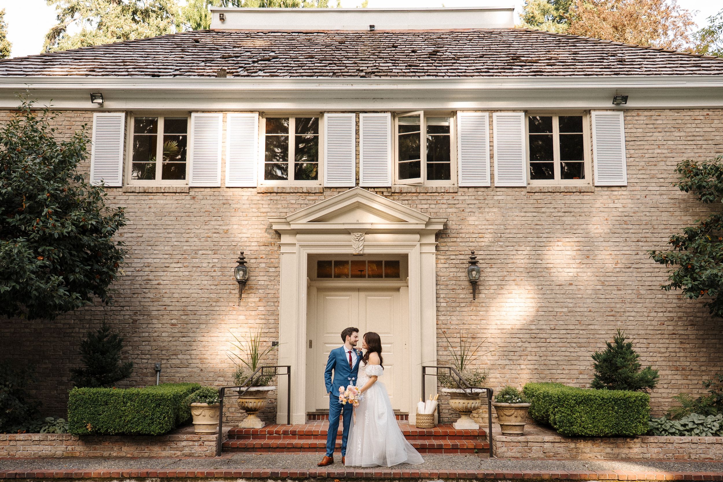 Beautiful wedding couple poses outside a grand historic estate with stone columns and classic architecture.
