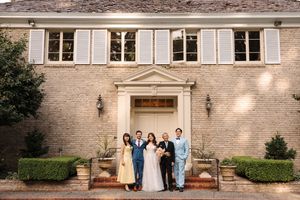 Wedding party members stand on stone steps in front of a church or historic building during a formal celebration.