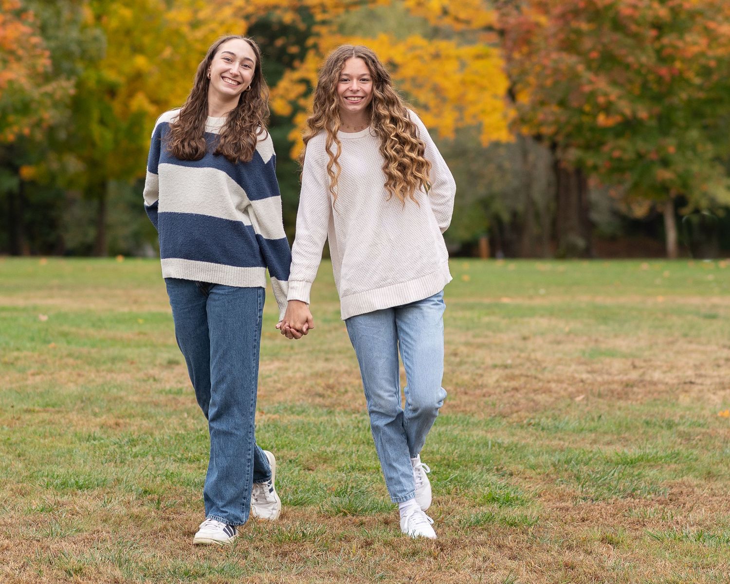 Two people walk through a vibrant autumn park with yellow and orange fall foliage in the background.