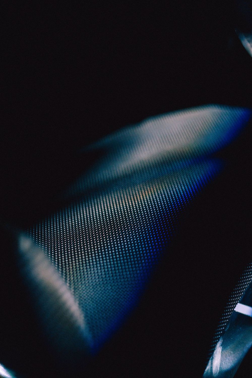 Abstract macro photograph showing a curved blue mesh or grid pattern fading into darkness.