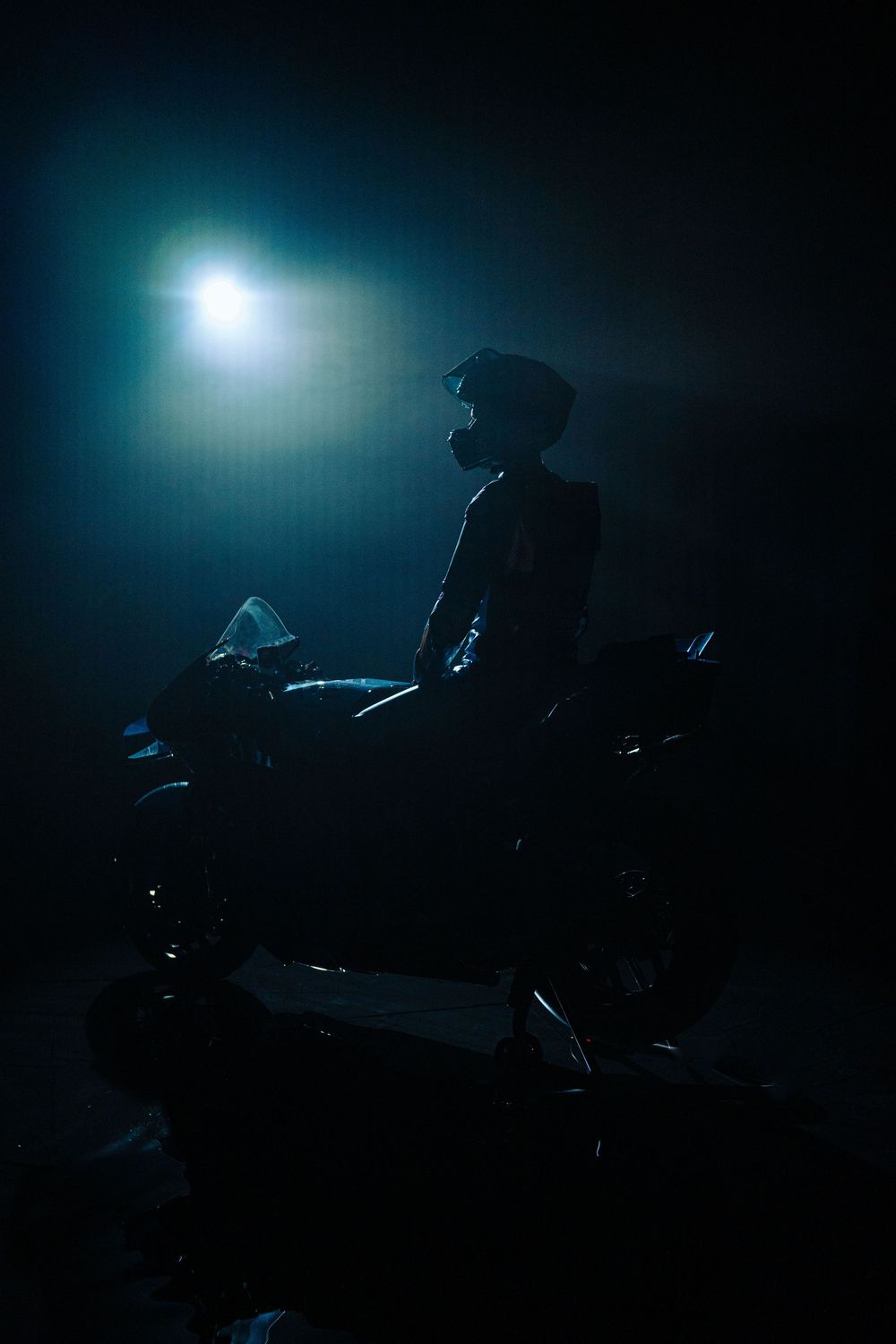 Silhouetted figure performs on a dark stage with dramatic blue backlighting creating a moody atmospheric effect.