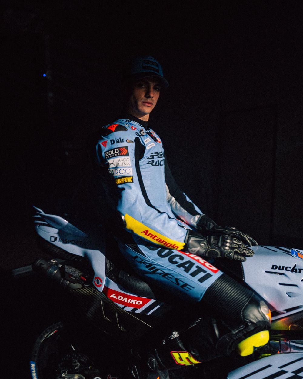 A white Ducati motorcycle with racing livery is shown in dramatic low-light conditions with red and yellow accents.