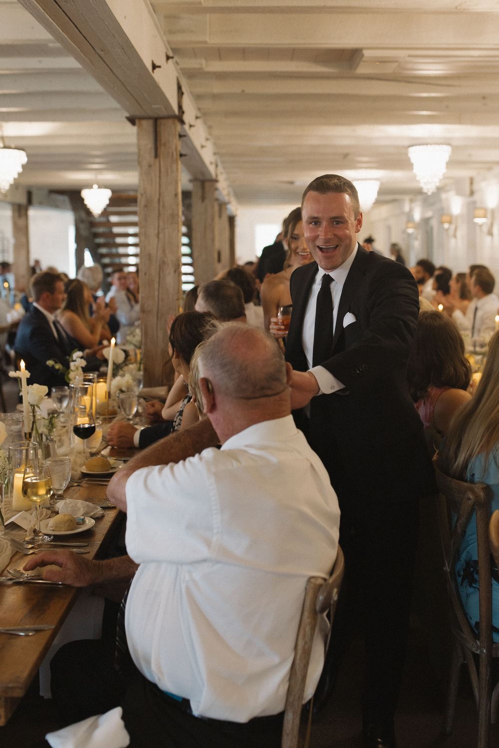 Wedding guests dancing and celebrating in an elegant indoor reception venue with chandeliers.