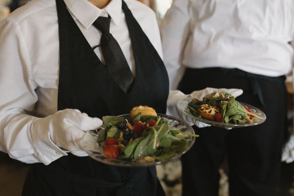 Servers in formal attire carry plates of food during an elegant wedding reception.
