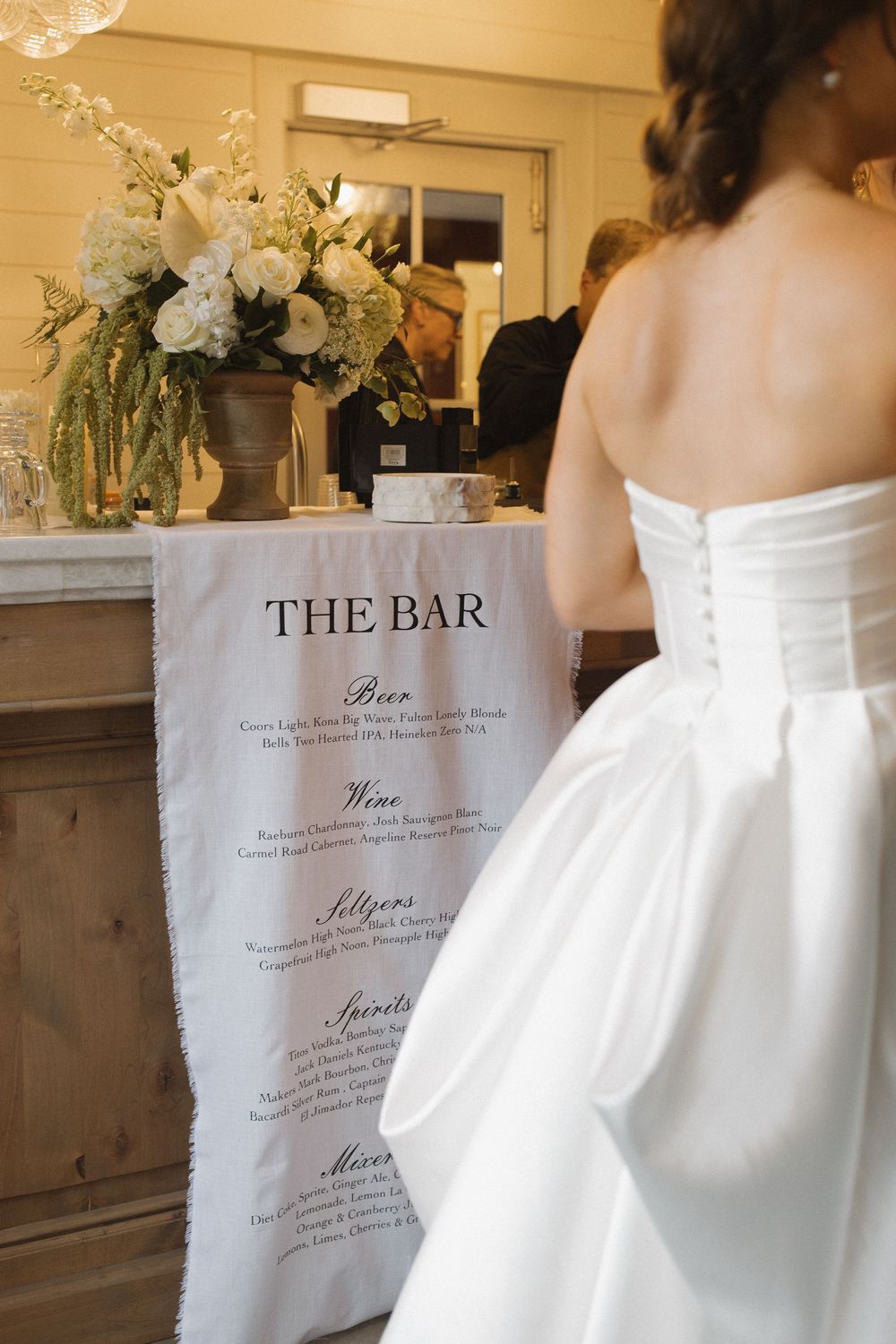 Wedding reception bar menu and decor with elegant white floral arrangements.