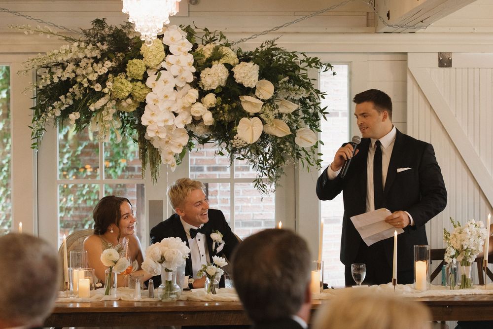 Wedding reception guests seated at elegant tables with white floral centerpieces and candlelight.