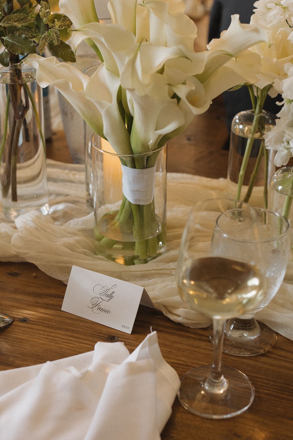 Elegant table setting with white floral arrangements and place cards at a wedding reception.