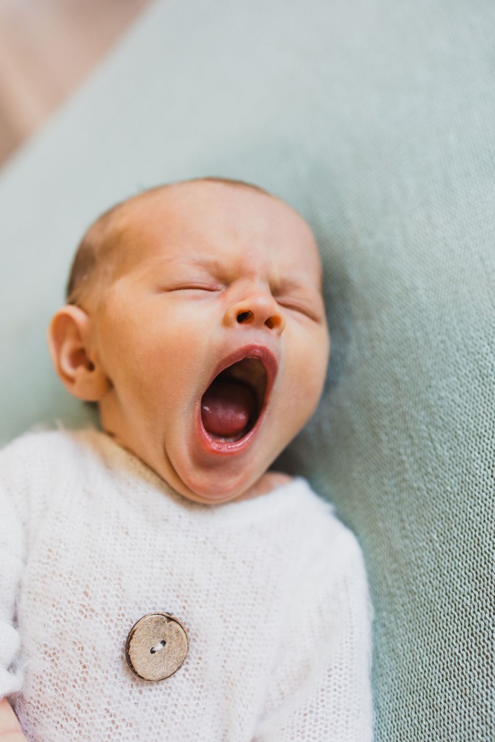 Series of a yawning newborn in white knit sweater.