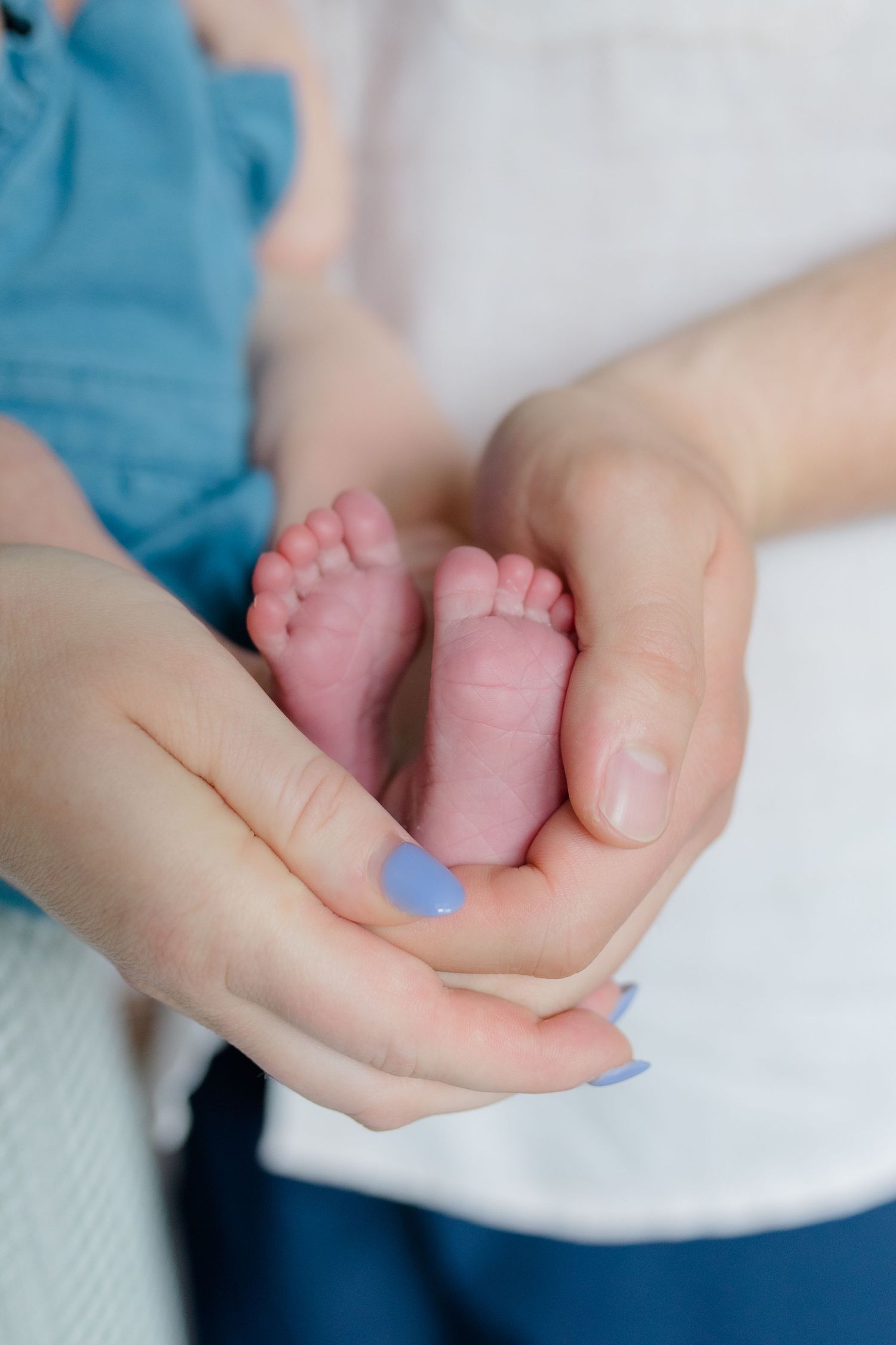 Gentle hands cradling tiny newborn feet with blue painted nails.