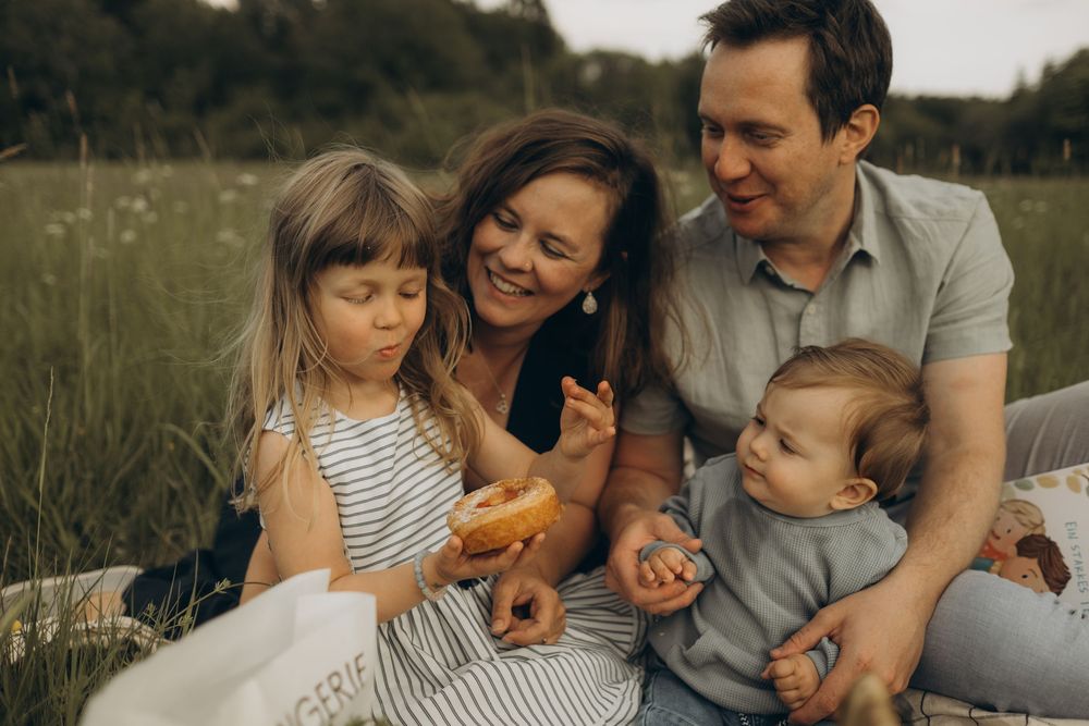 family of 4 eating picnic in summer field during natural style family photo session in Stockholm