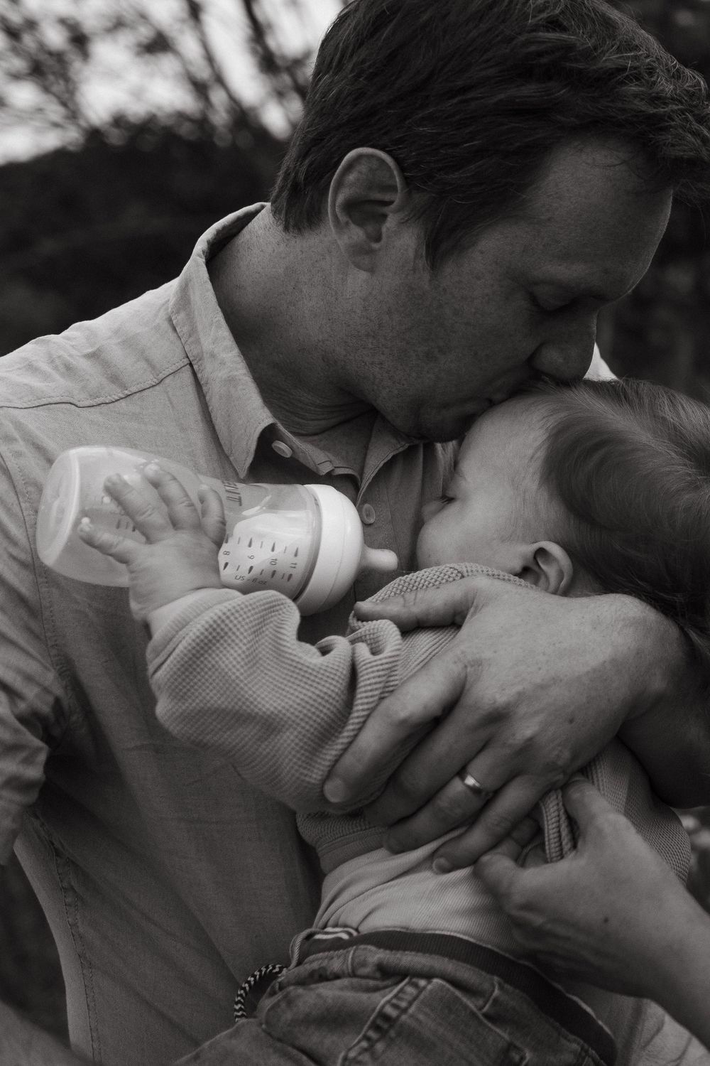 father kissing baby's forehead during feeding while being captured by candid style family photographer in Stockholm