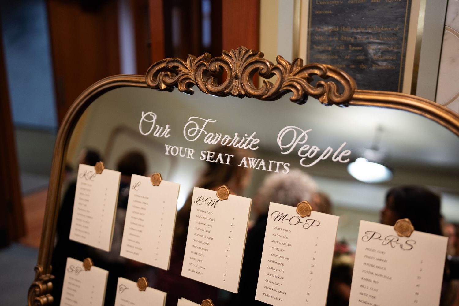 A rustic wedding seating chart display with elegant calligraphy text on multiple white paper scrolls against a dark wall.