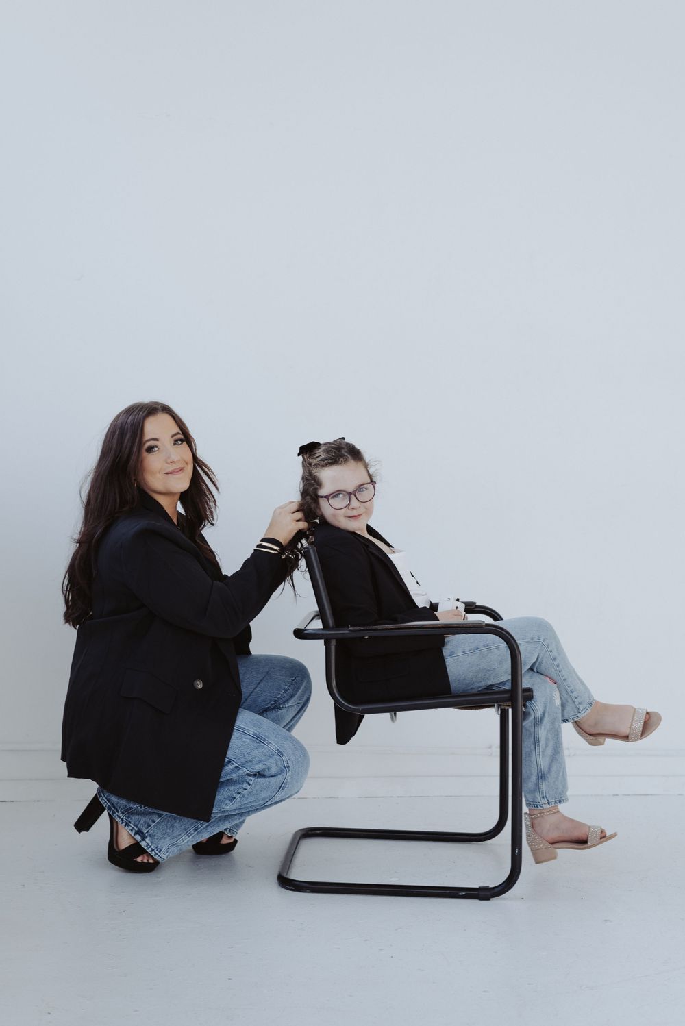 Playful interaction with black chair in casual denim and dark jacket ensemble.