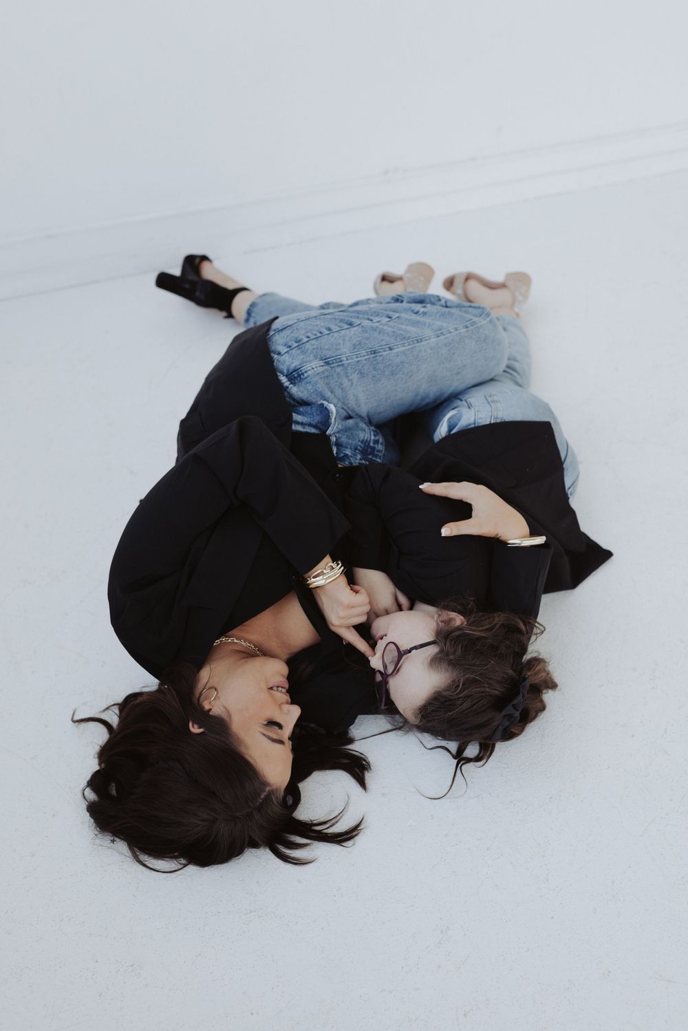 Artistic overhead shot of couple lying on white floor in casual black and denim outfits.