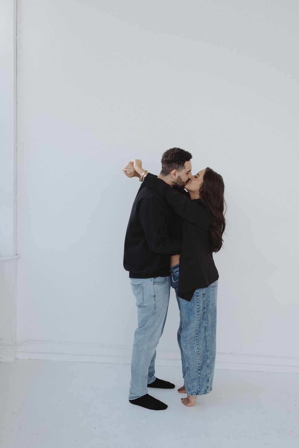 Intimate couple photoshoot against white wall showing playful dance-like poses.