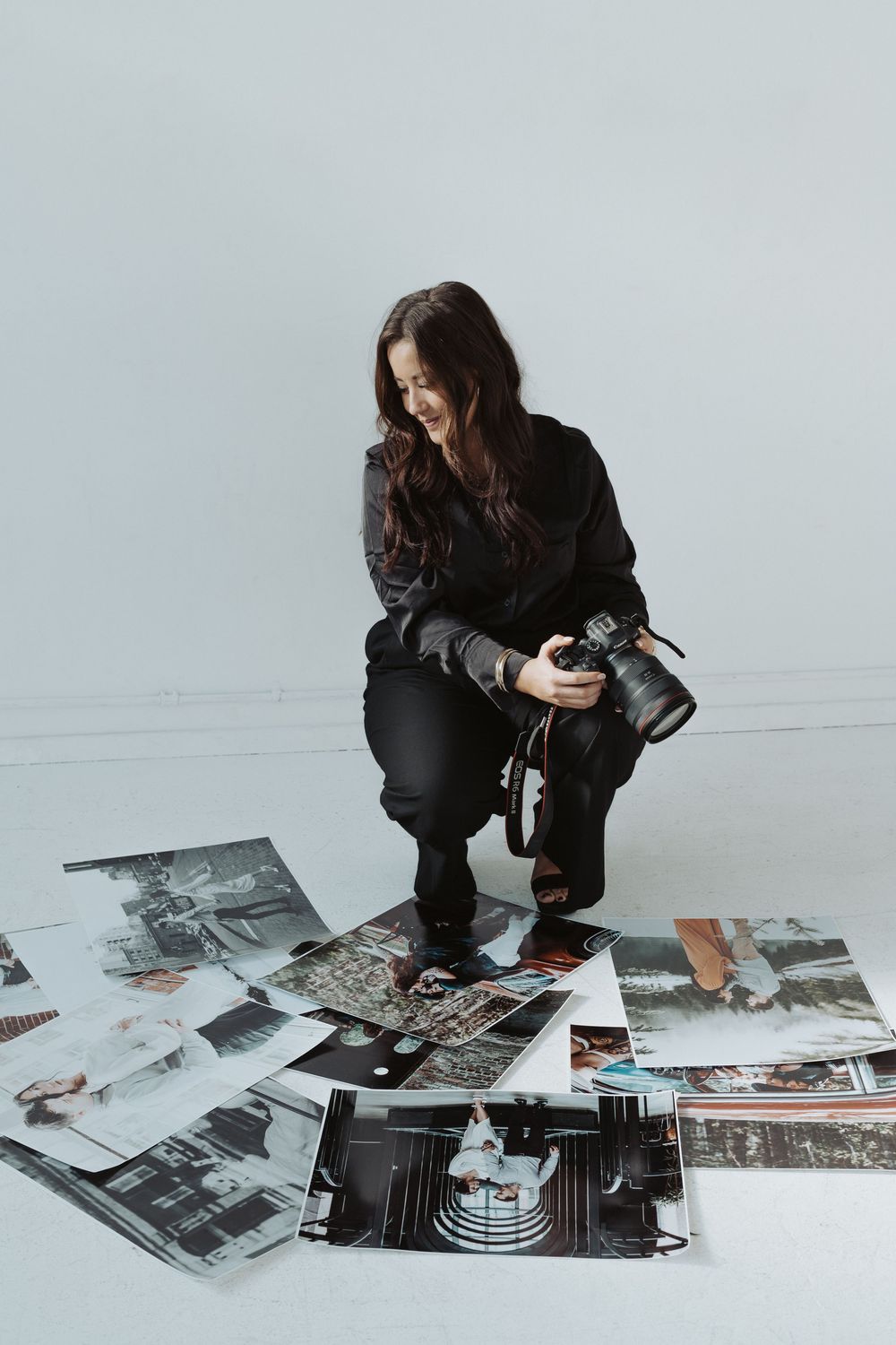 Person in black examining photographs and vintage camera equipment spread on white floor.