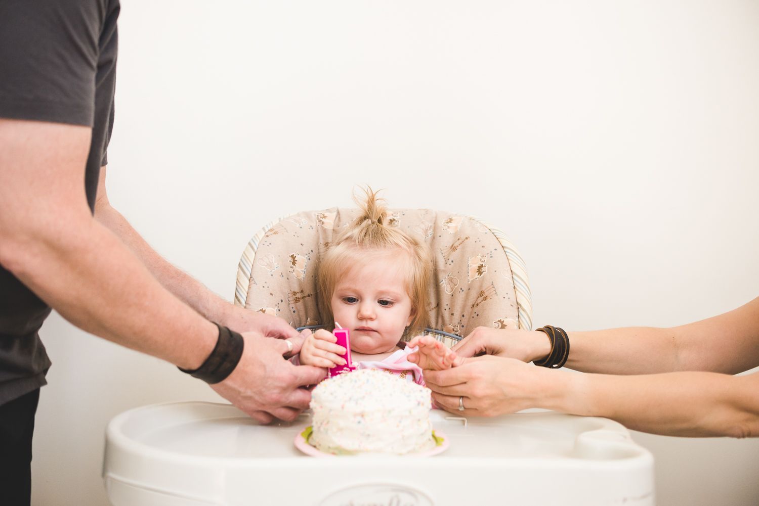 Small hands reaching for a frosted cake with decorative flowers on top in a light studio setting.