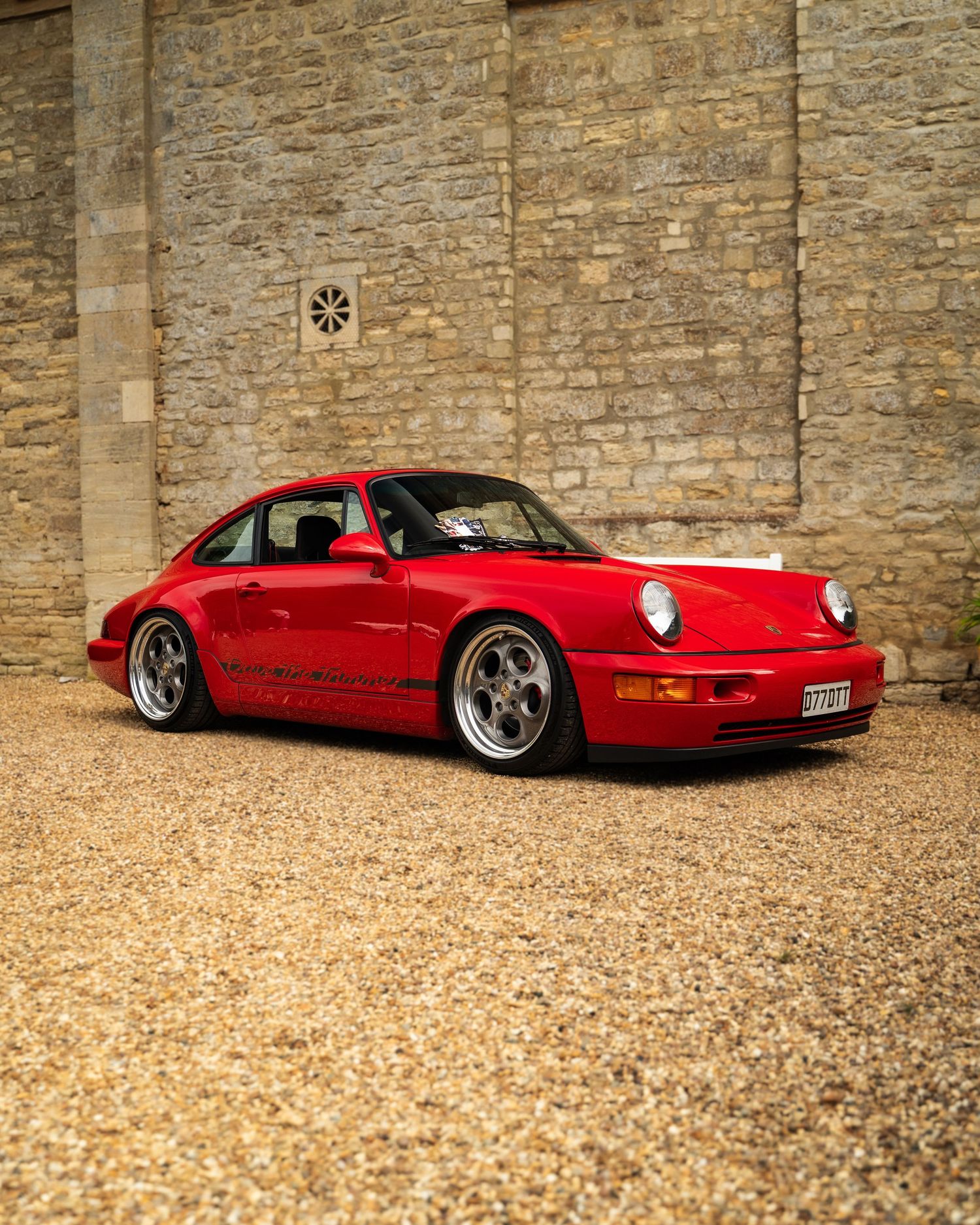 Red classic Porsche photographed against stone wall in dramatic low angle.