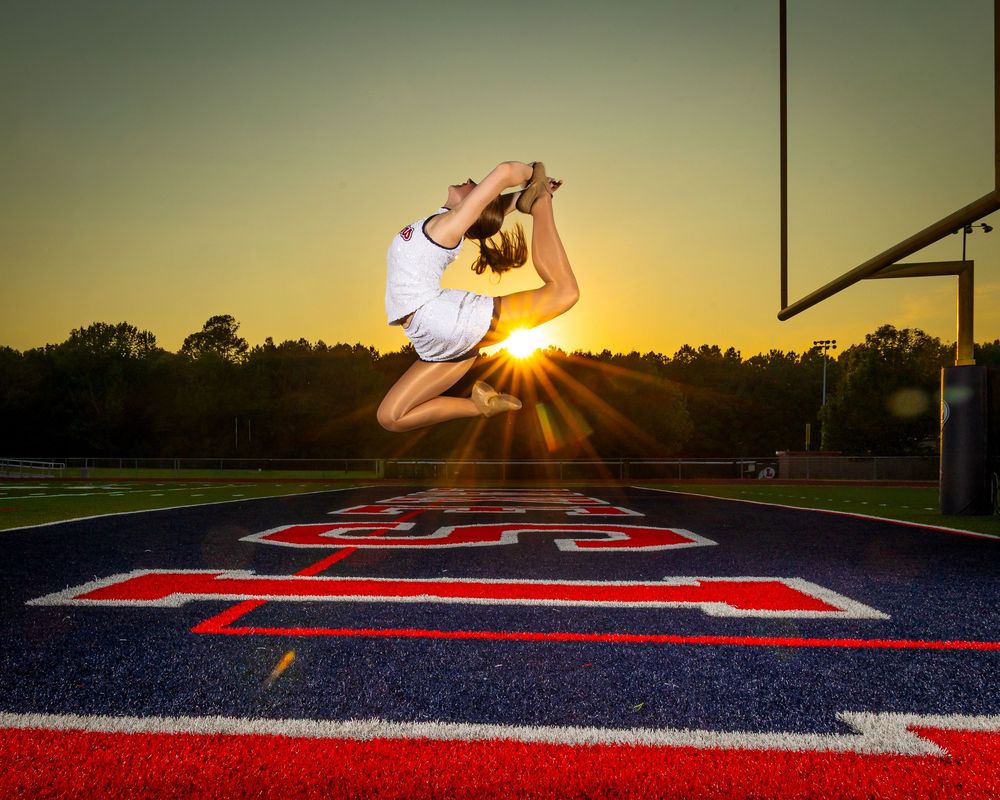 A series of cheerleading jumps photographed at sunset on a football field with red and blue turf.