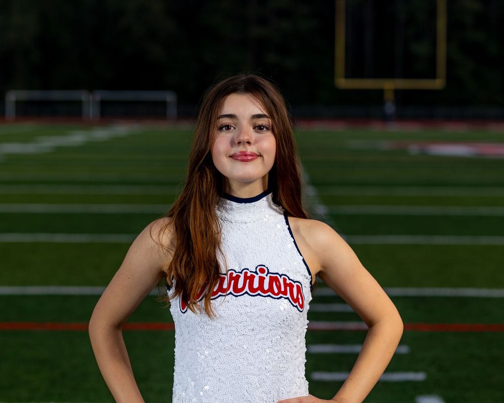 Cheerleader in white uniform poses confidently on sports field during evening photoshoot.