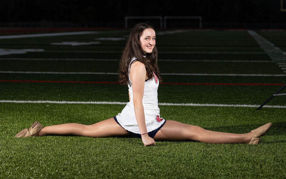 Cheerleader performs a full split on green athletic field grass in outdoor stadium.