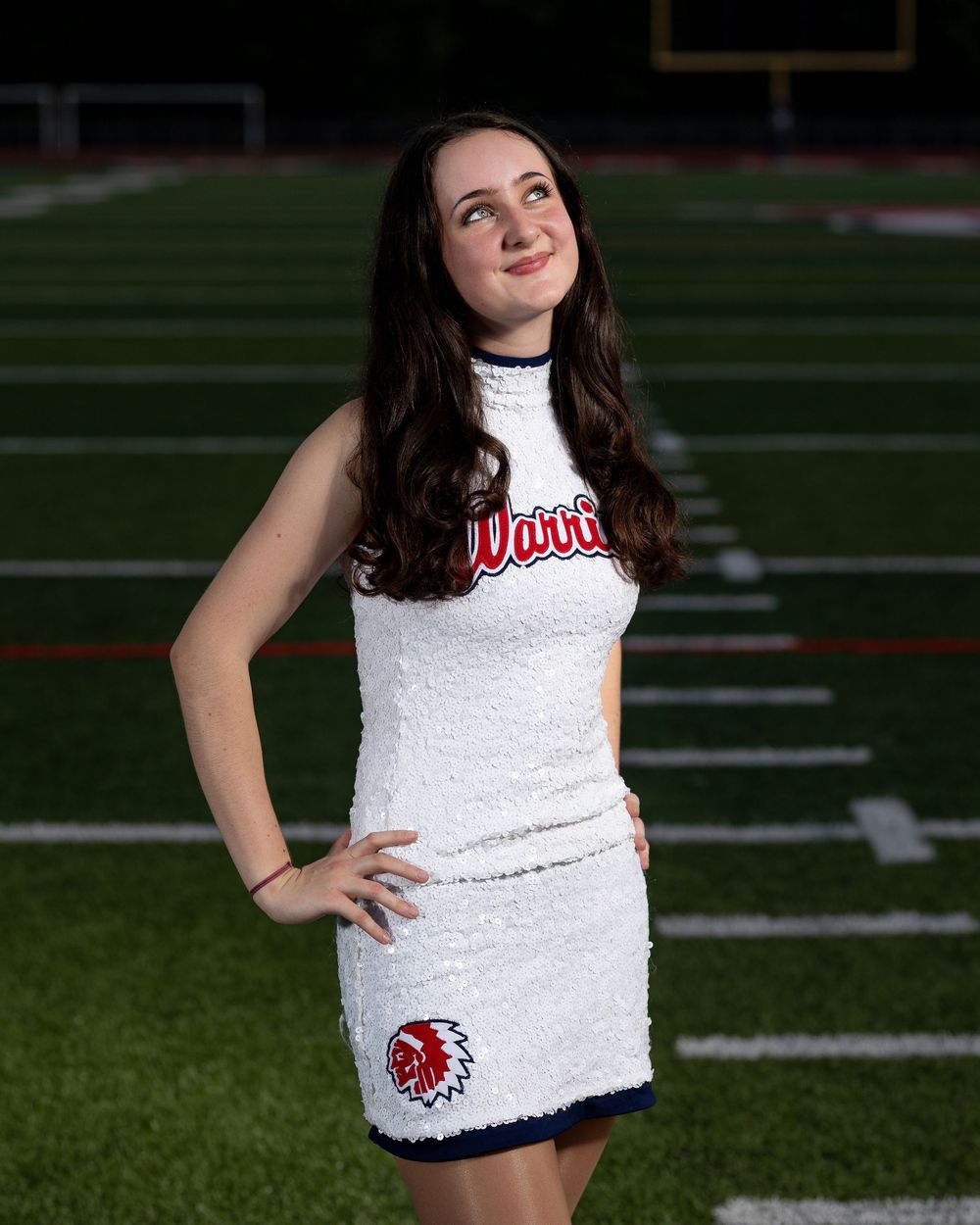 Cheerleader in white uniform poses on football field during photo session at night.