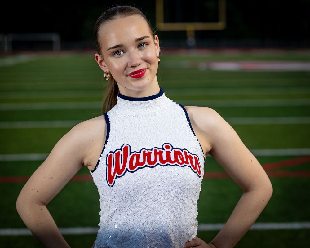 Cheerleader uniform detail showing white sequined top with Warriors text against football field background.