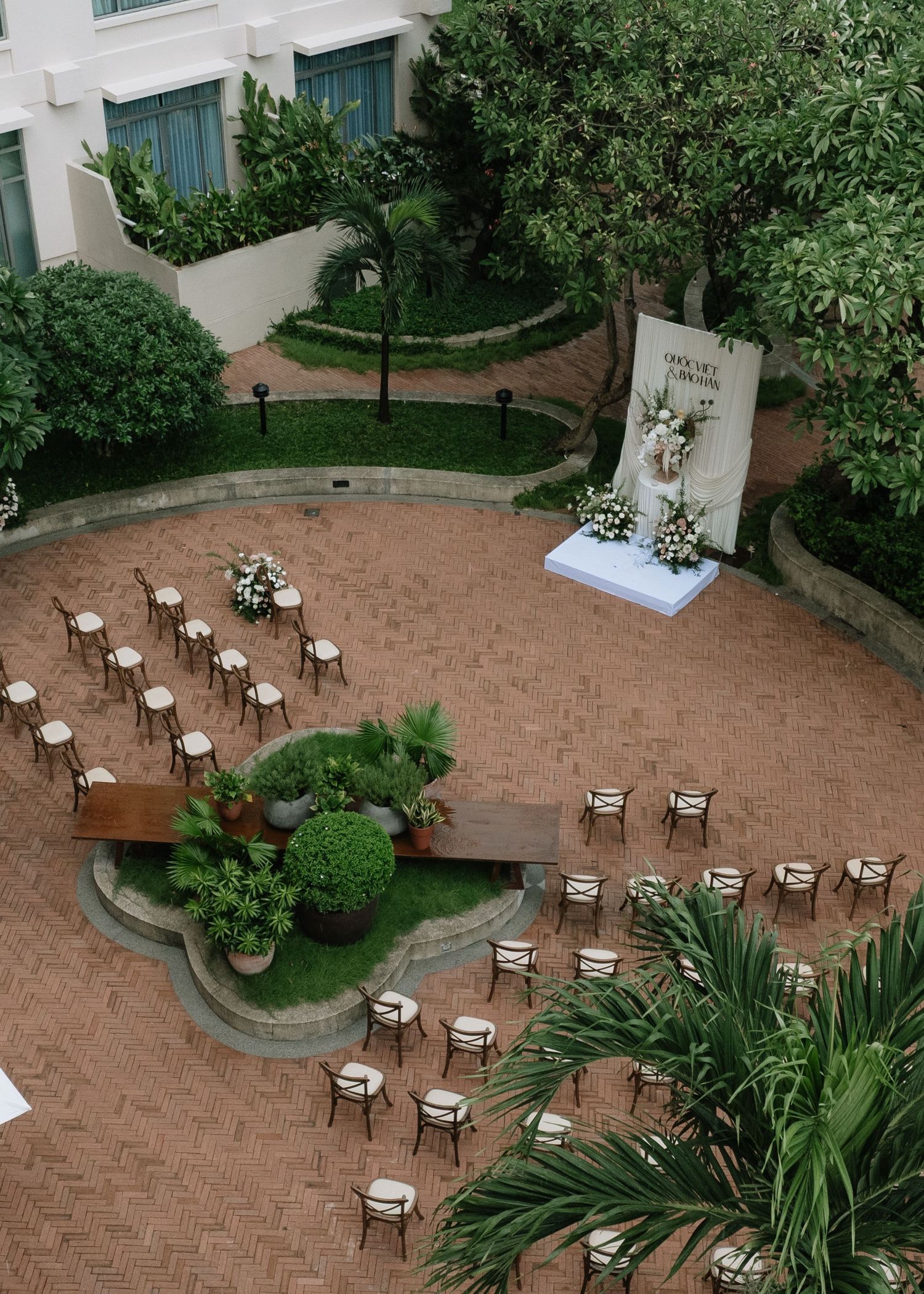 Aerial view of outdoor wedding ceremony setup with rows of chairs and floral backdrop in garden.