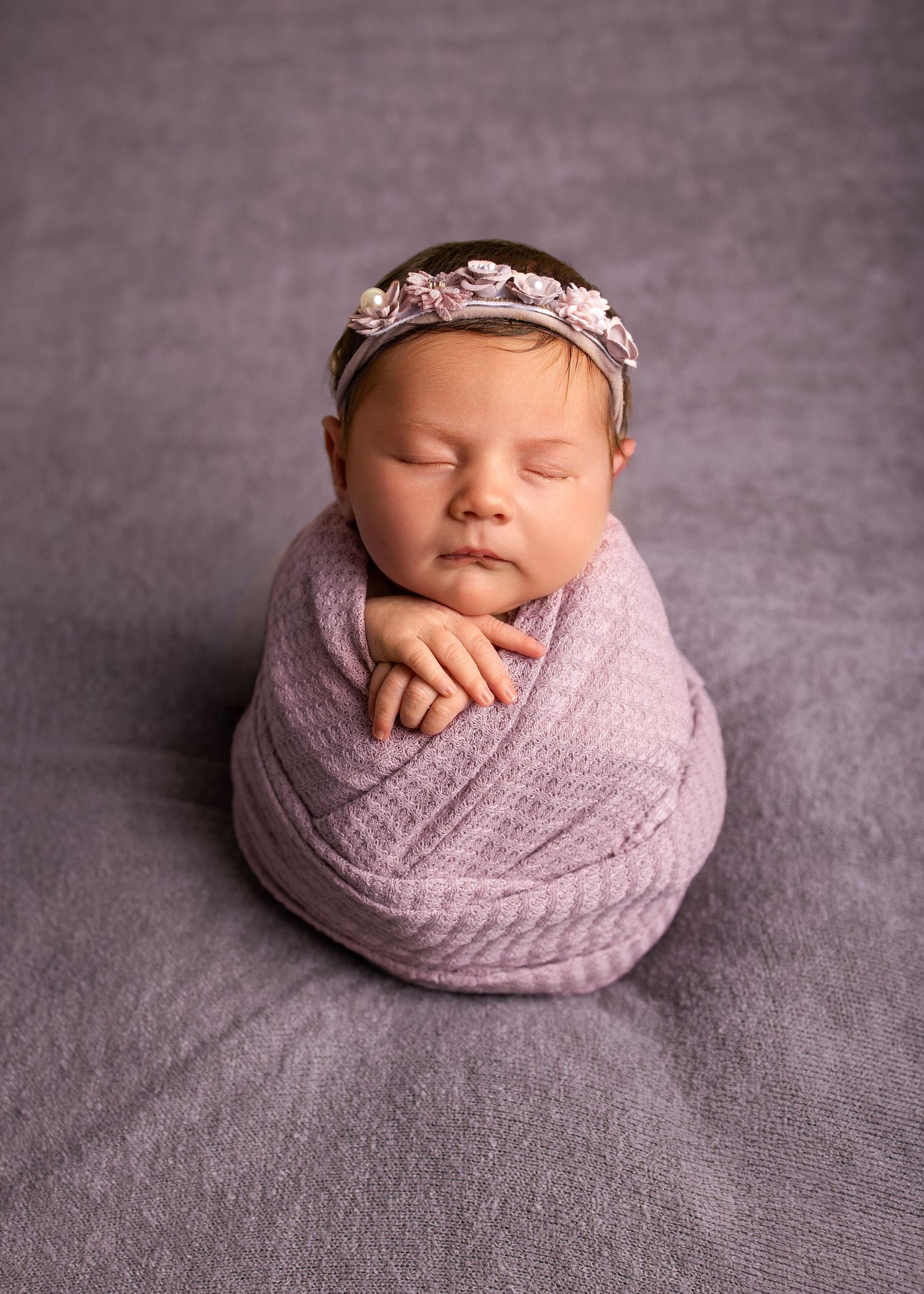 Sleeping newborn in soft turquoise floral accessories and headpiece on cream backdrop during professional photo session.