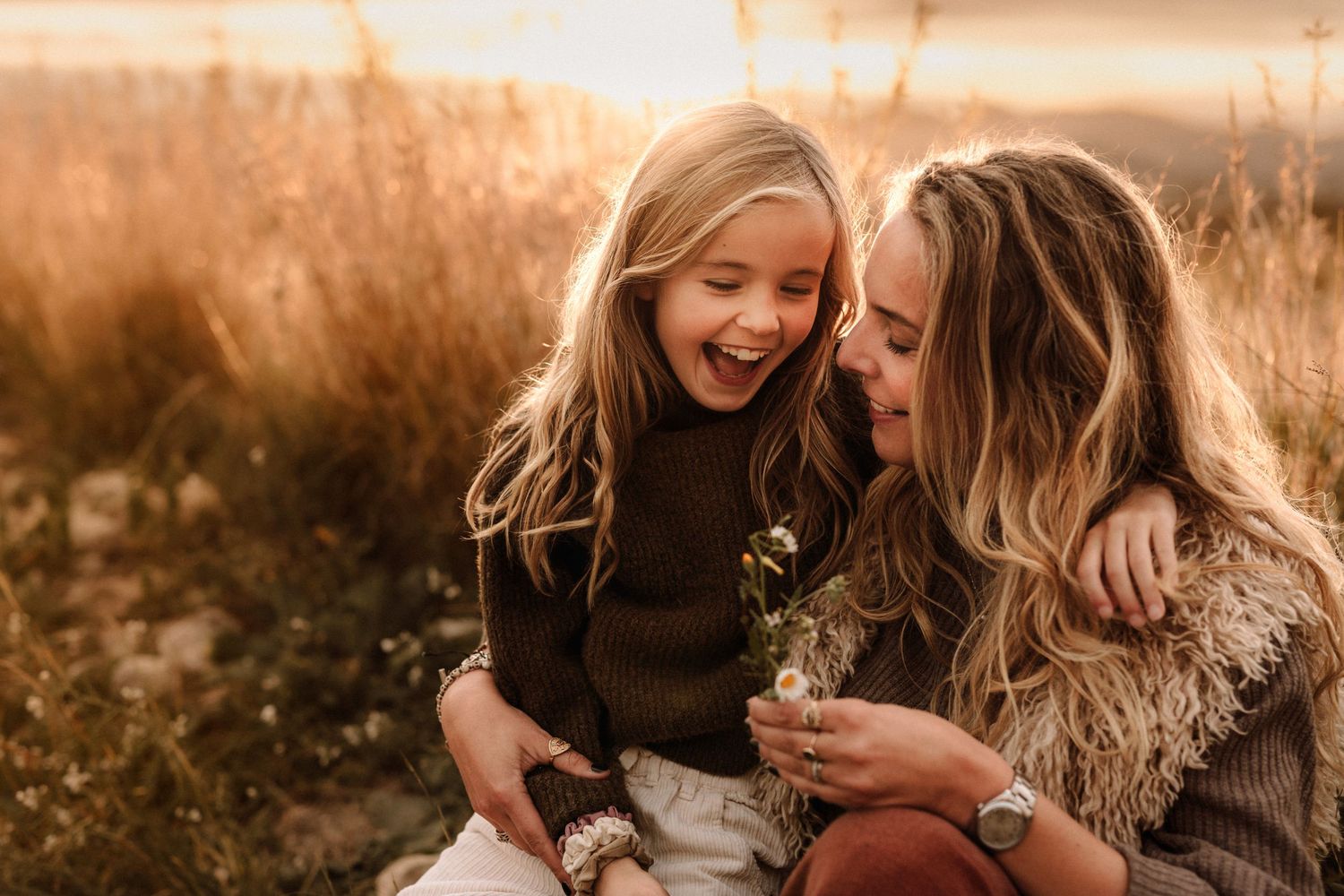 A joyful bonding moment between parent and child sitting in a golden sunlit meadow during sunset for a family session in Javea,