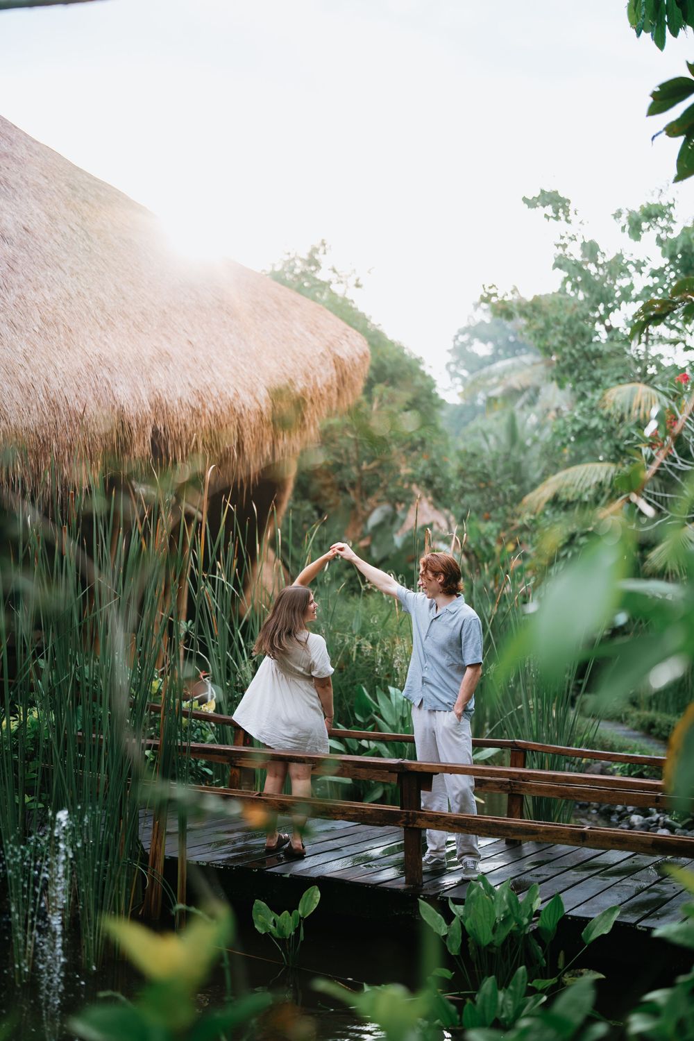 A couple dances on a wooden deck surrounded by tropical plants and thatched roof structures.