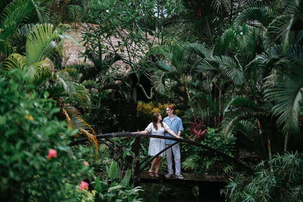 A romantic couple moment captured on a wooden walkway amidst tropical greenery.