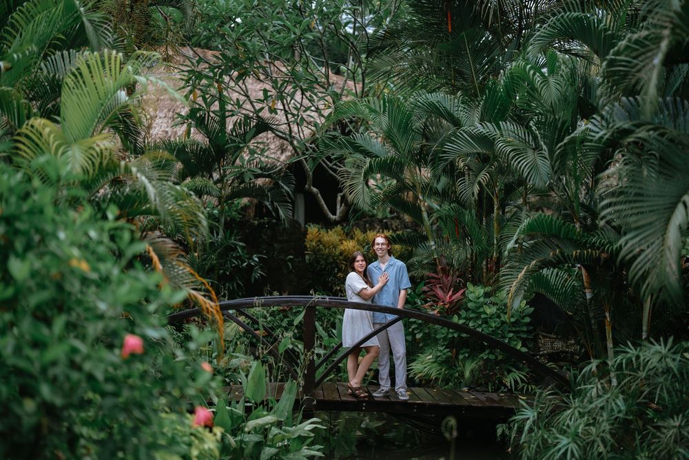 Couple embraces on an elevated wooden pathway surrounded by tropical plants and flowers.