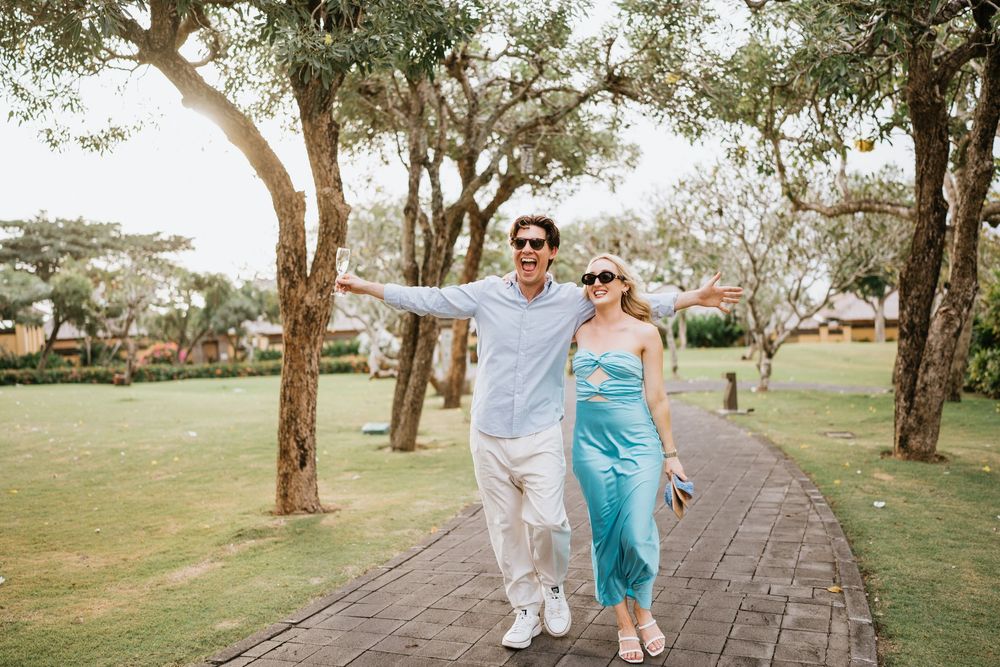 A couple strolls down a scenic pathway surrounded by lush trees and greenery.