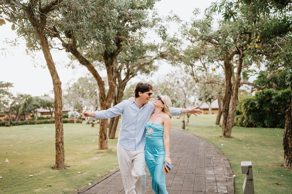 Two people walking hand in hand along a peaceful garden path with trees overhead.